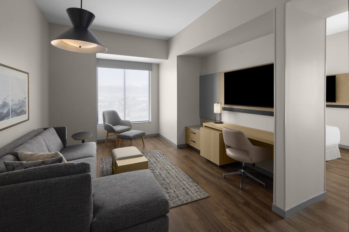 Una sala moderna con un sofá, un escritorio, una silla, un televisor y un ventanal grande.