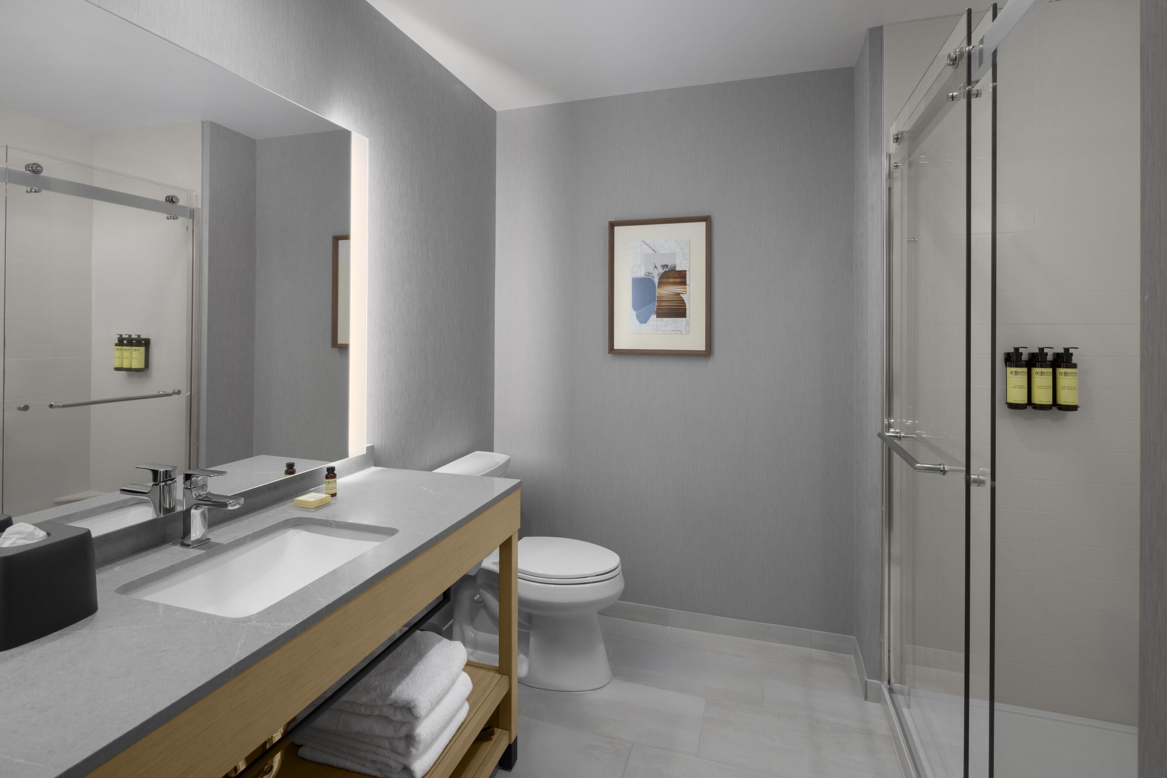 A modern bathroom with a large mirror, a sink, a toilet, and a shower.