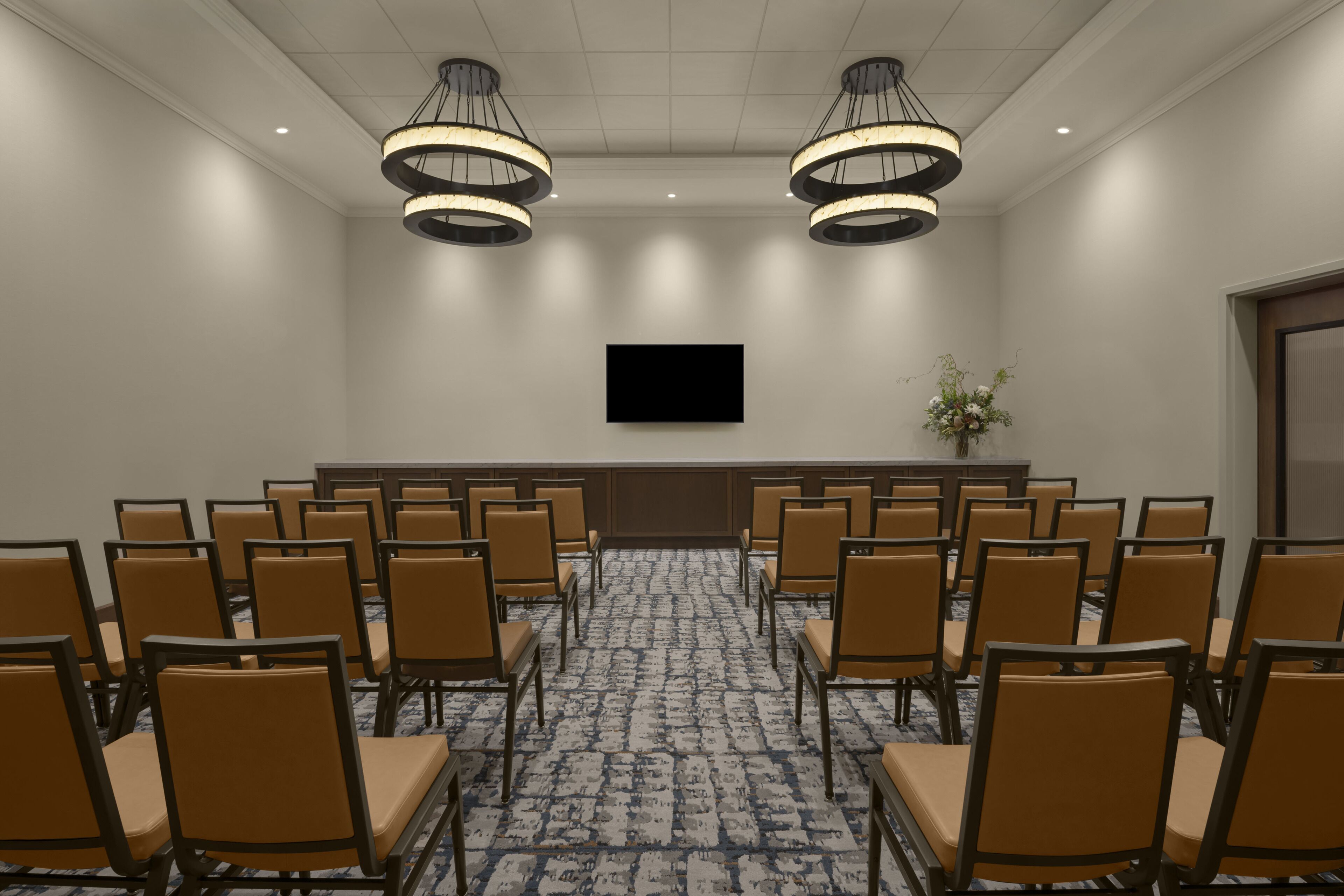 Een vergaderzaal met een lange tafel, stoelen, een flatscreen televisie en twee kroonluchters.