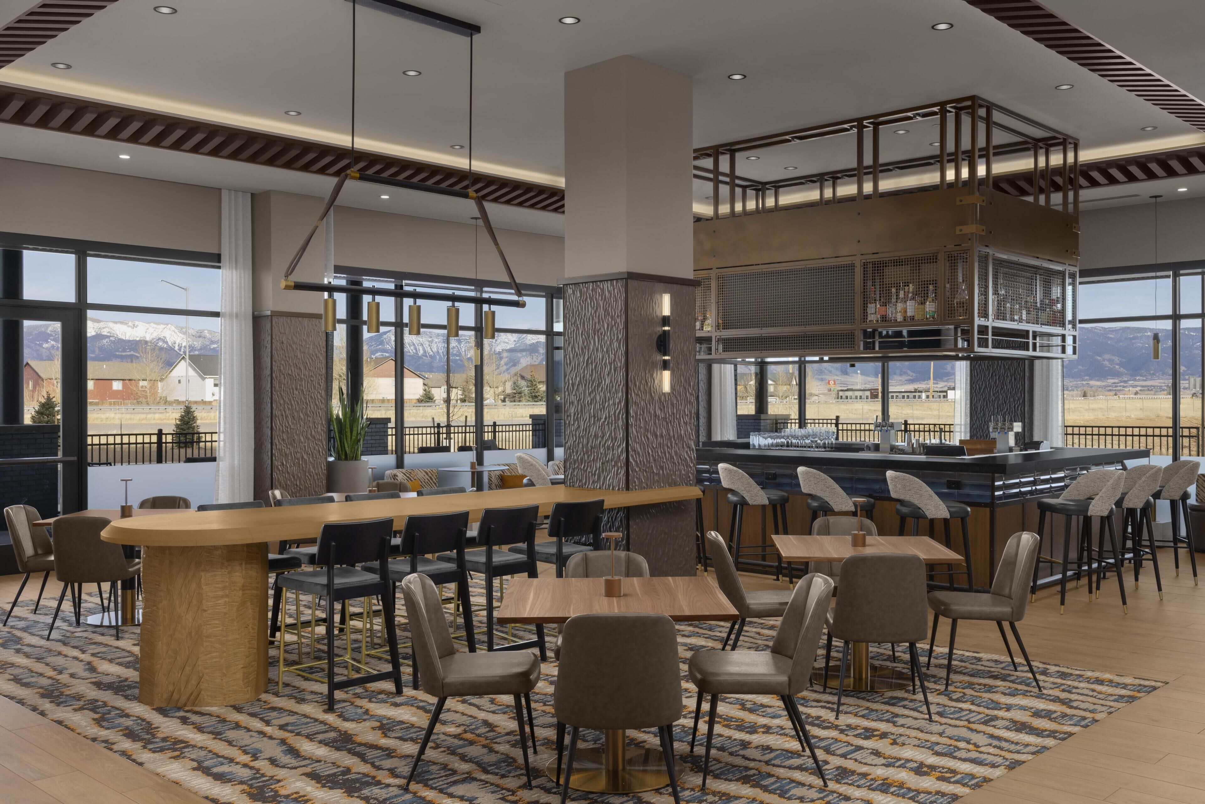 A modern bar area with a high ceiling, large windows, and a view of the mountains.