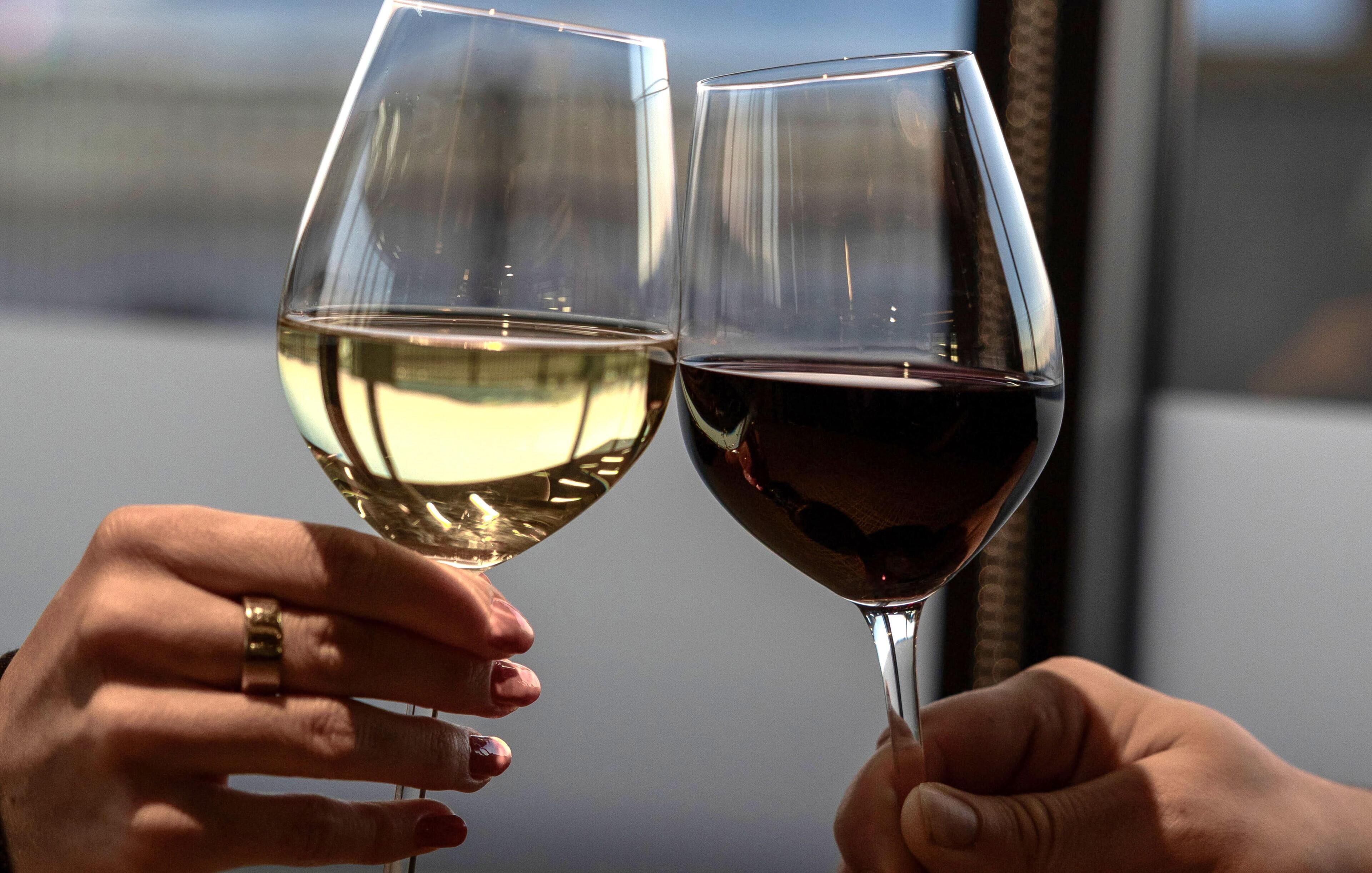 Deux mains tenant des verres à vin, l’une contenant du vin blanc et l’autre du vin rouge, sur un arrière-plan flou.