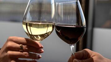 Deux mains tenant des verres à vin, l’une contenant du vin blanc et l’autre du vin rouge, sur un arrière-plan flou.