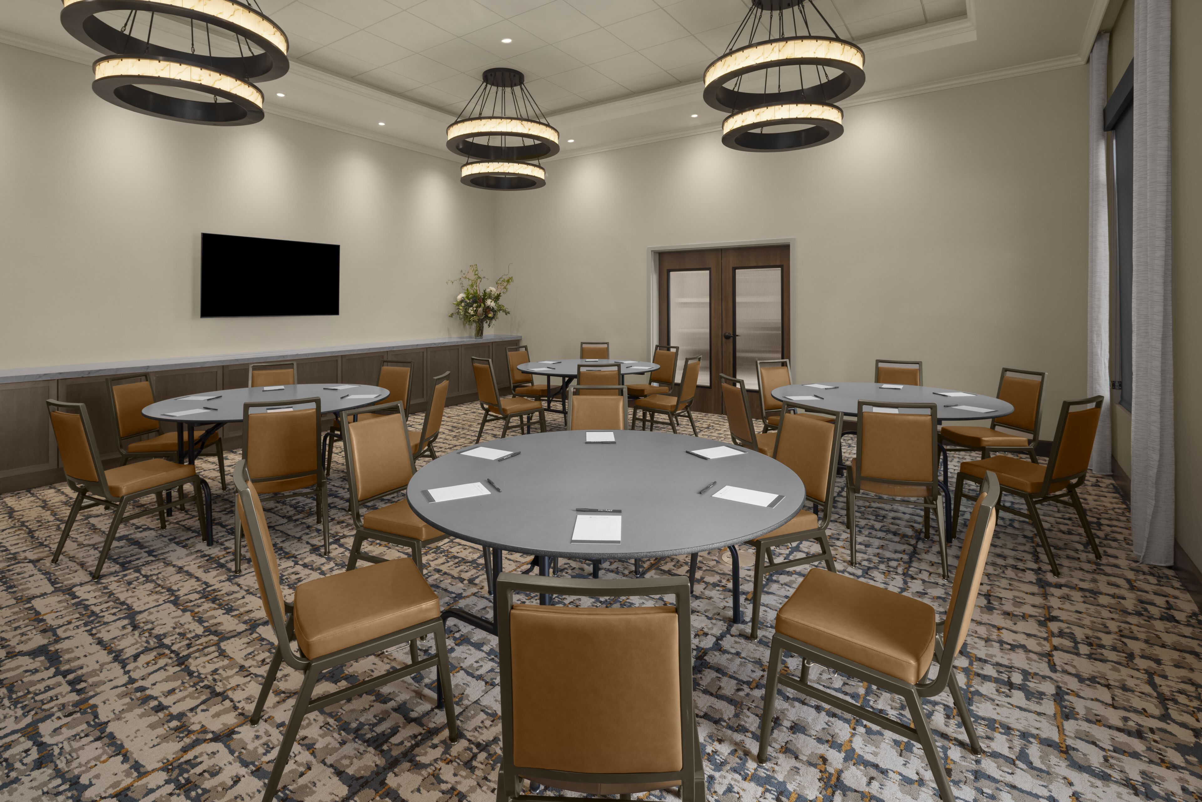 Une salle de conférence équipée de plusieurs tables et chaises, d’un téléviseur à écran plat et d’une moquette à motifs.