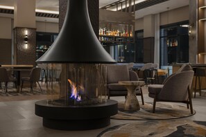 Un área de lounge moderna con una chimenea central, asientos y un bar al fondo.
