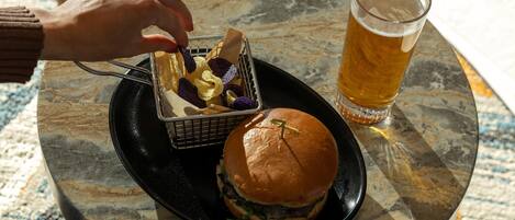 A meal consisting of a burger, a basket of chips, and a glass of beer on a table.