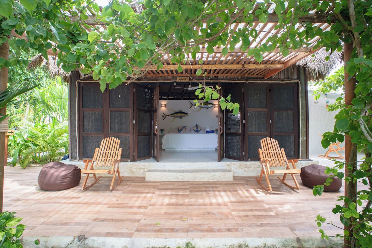 A traditional wooden structure with a thatched roof, a bed, and two wooden rocking chairs.
