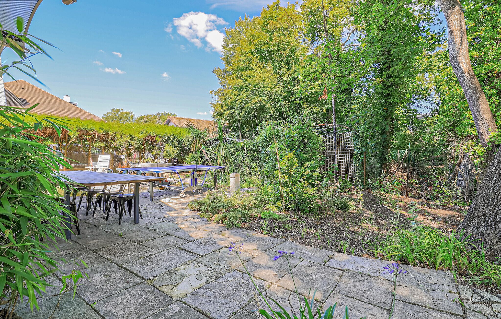 Un patio con mobiliario exterior, una pérgola y abundante vegetación.