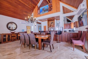 A spacious dining area with a wooden table and chairs, a chandelier, and a kitchen area with wooden cabinets and a countertop. - Villa Turquesa Luxe Beachfront Living with Stunning Ocean Views (San Pedro)