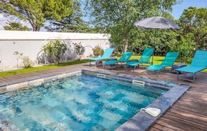 A swimming pool with clear water, surrounded by wooden decking and green lounge chairs. - Maison proche Alpilles (Arles)