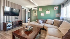 Una sala de estar con un sofá, una mesa de centro con adornos, un televisor sobre un mueble de madera y cuadros enmarcados en la pared.