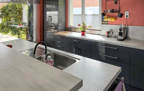 A modern kitchen with a stainless steel sink, black cabinets, and a window with a view. - Maison proche Alpilles (Arles)