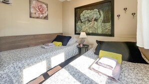 Habitación de hotel con dos camas, una mesita de noche, una lámpara y obras de arte en las paredes.