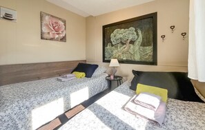 A hotel room with two beds, a nightstand, a lamp, and artwork on the walls. - Maison proche Alpilles (Arles)