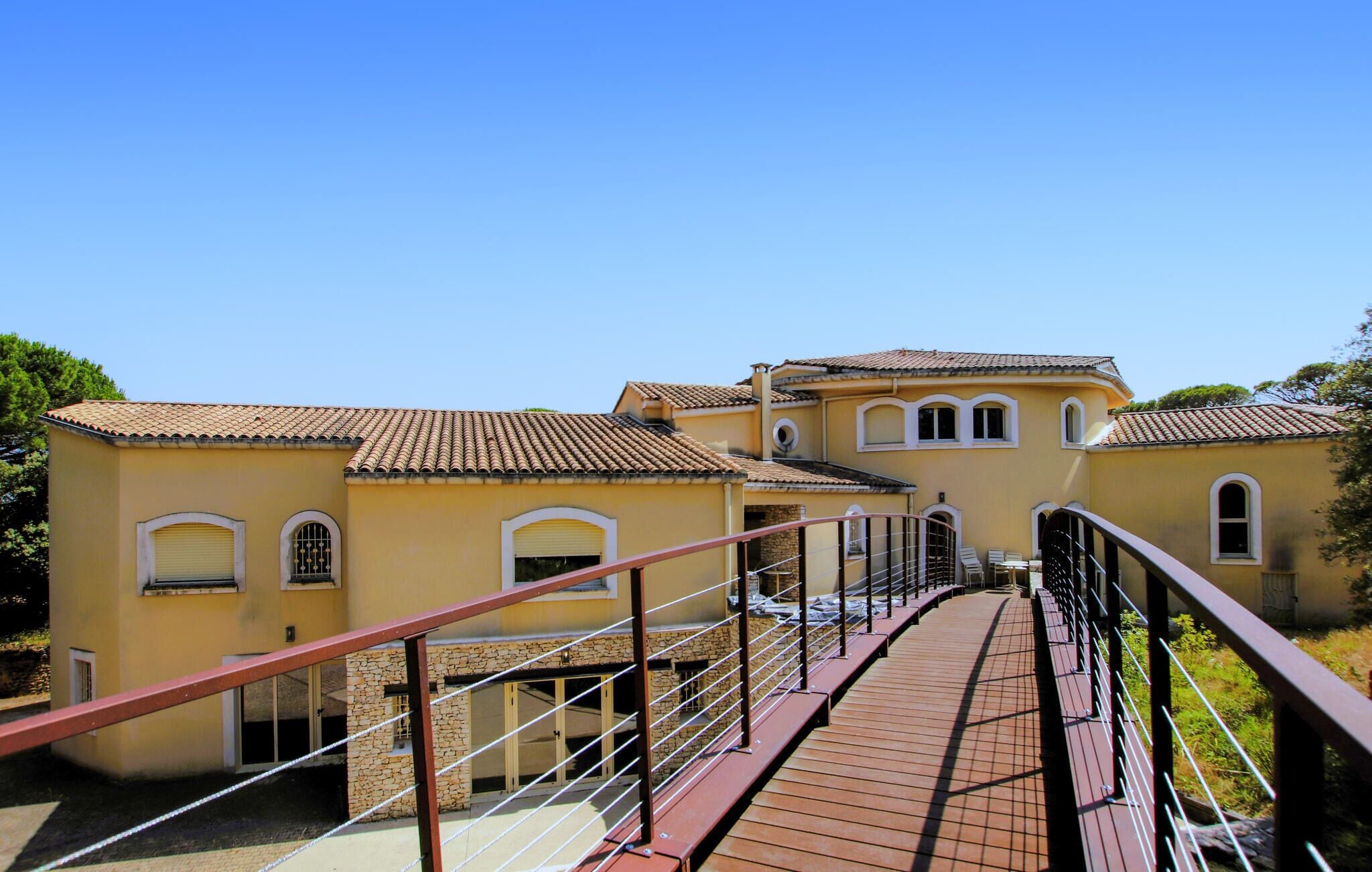 A yellow building with a tiled roof, a stone wall, and a wooden bridge with metal railings.