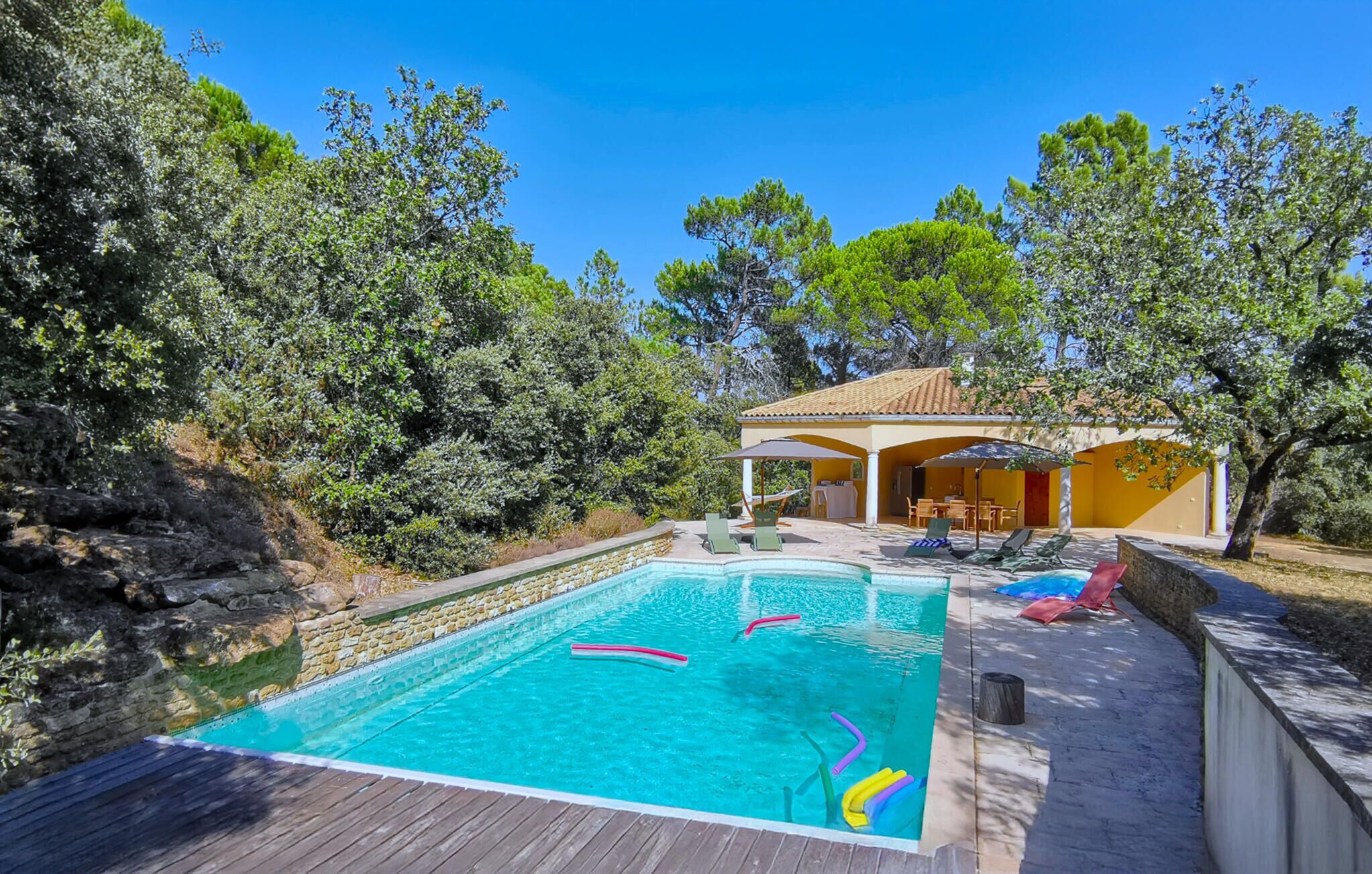 A pool area with a wooden deck, lounge chairs, and a covered seating area.