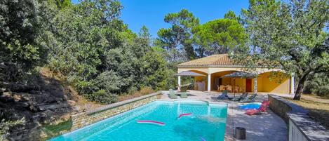 A pool area with a wooden deck, lounge chairs, and a covered seating area.