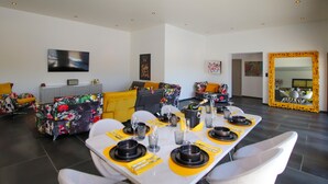 A dining area with a long table set for six, surrounded by modern sofas with floral upholstery. - Cozy home in Montboucher sur Jabron (Montboucher sur Jabron)