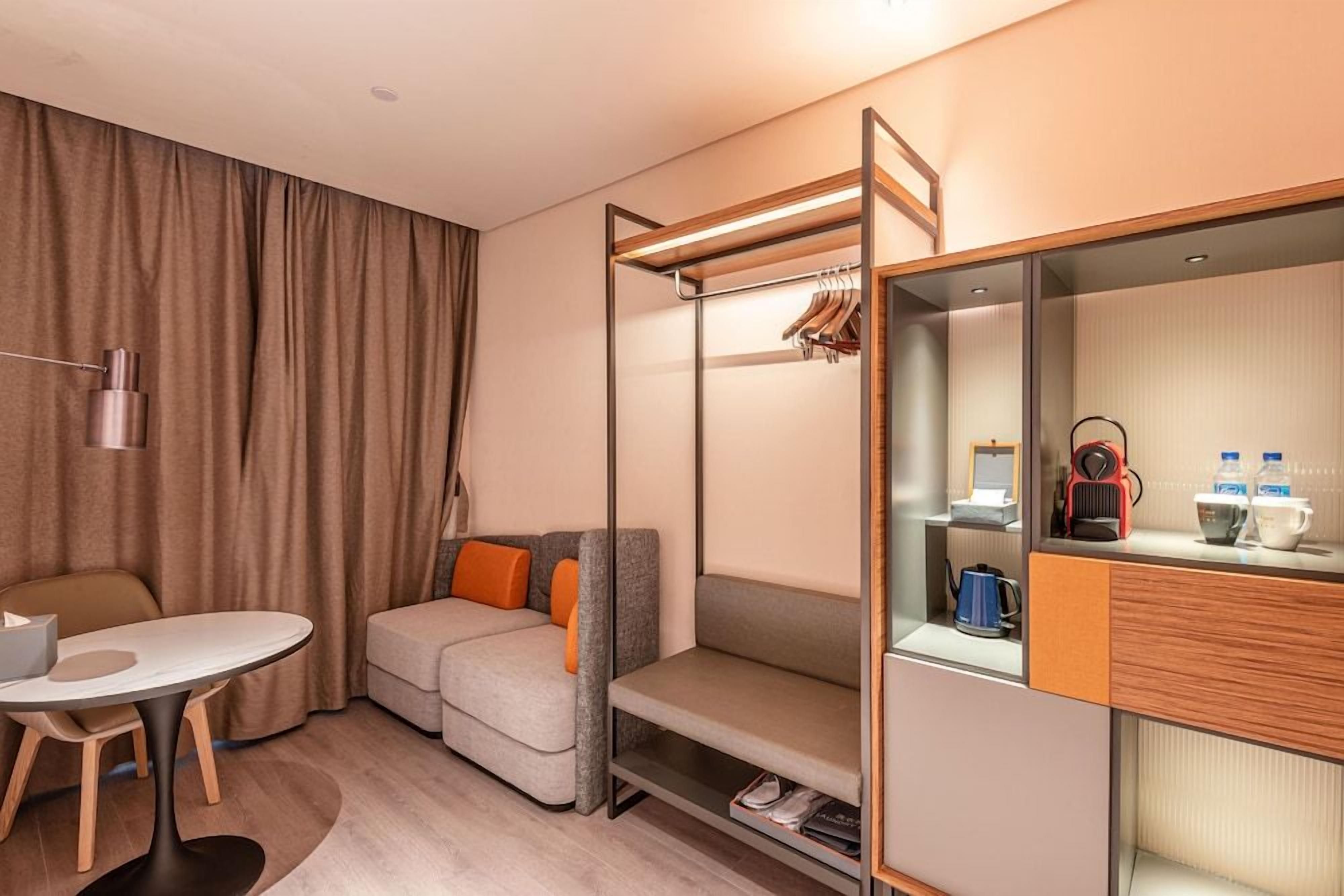 Une chambre d’hôtel compacte comprenant un lit superposé, un petit canapé, une table et un coin cuisine.