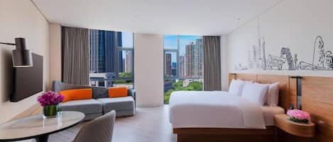 A modern hotel room with a bed, sofa, and a desk with a chair.