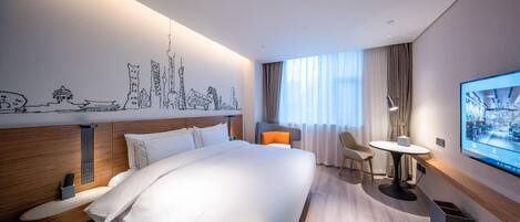A hotel room with a large bed, a desk with a chair, a TV, and a wall with a cityscape drawing.
