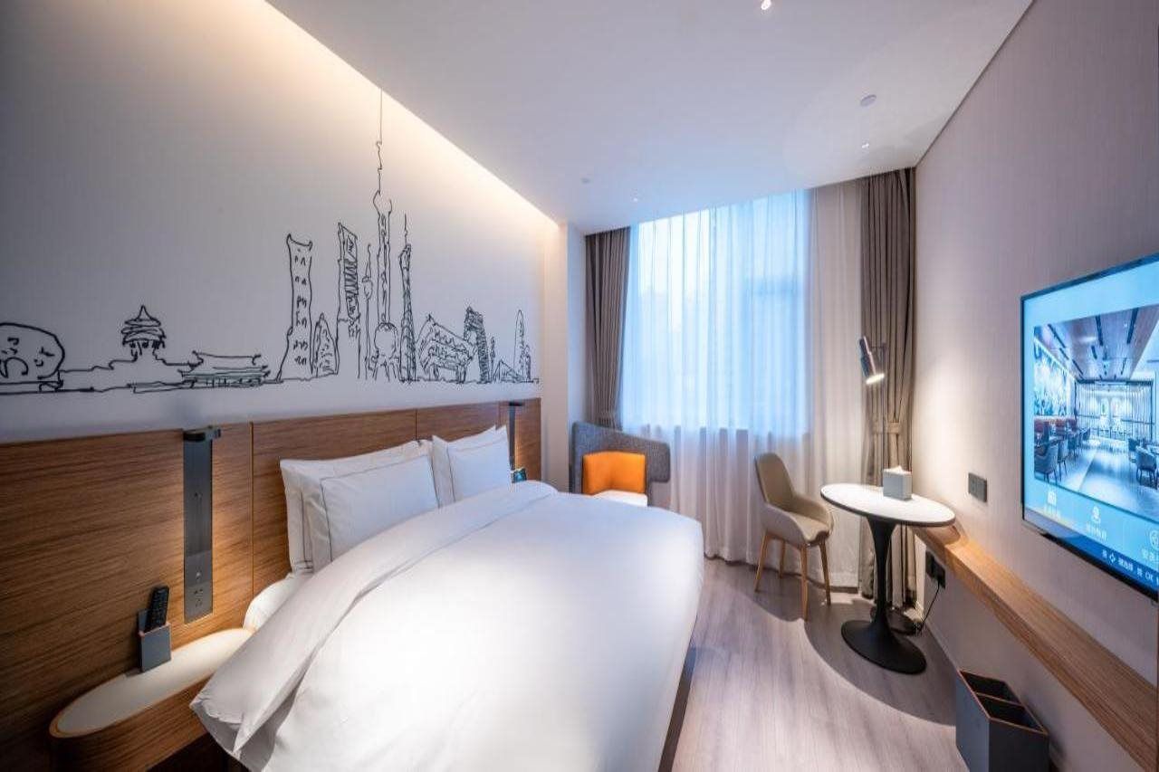 Habitación de hotel moderna con una cama grande, un escritorio, una silla y un mural con un paisaje urbano en la pared.