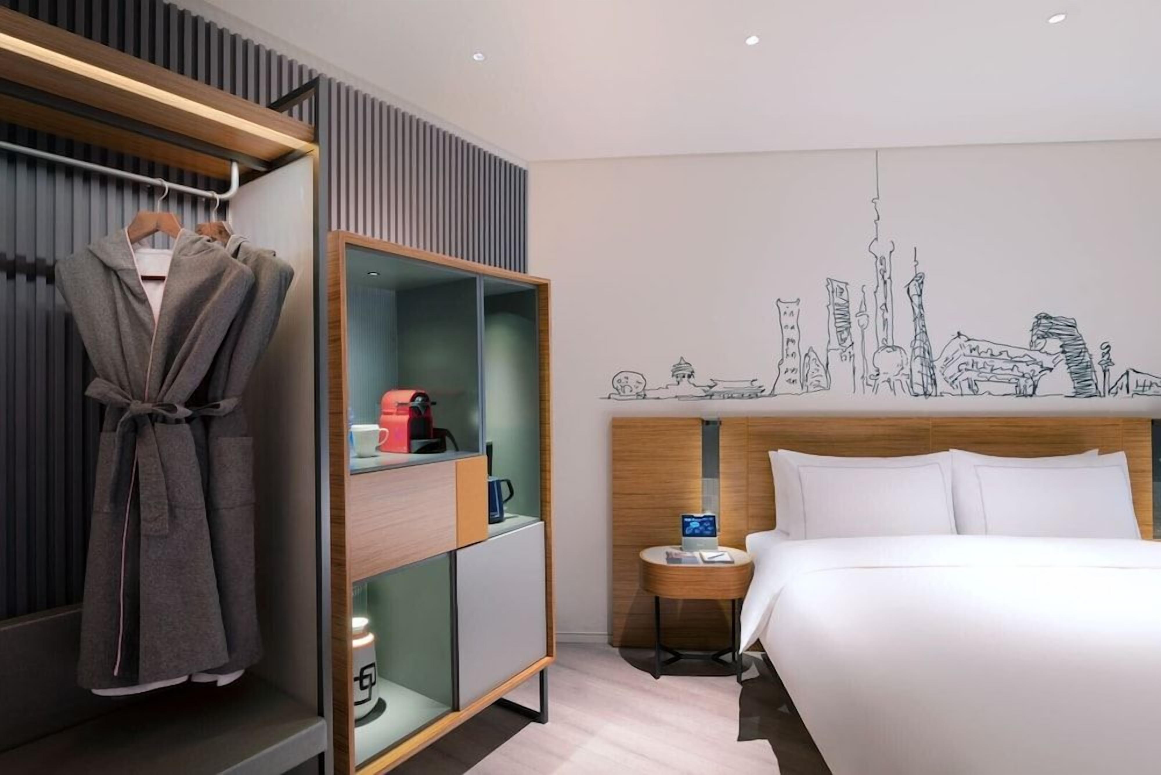 Habitación de hotel con cama, armario, mesita de noche y un mural con vista a la ciudad.