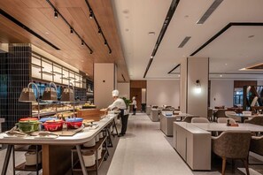 A modern restaurant with a long counter, multiple tables, and a chef preparing food.