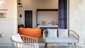 Quarto com cama, duas cadeiras de vime, um pufe laranja e uma mesa de vidro.