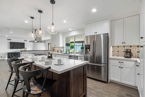 A modern kitchen with white cabinets, a large stainless steel refrigerator, and a central island with bar stools. - Adobe Modern - House with Private Pool in Scottsdale (Scottsdale)