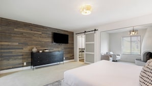 Quarto com cama grande, penteadeira, TV fixada na parede e porta de armário deslizante.