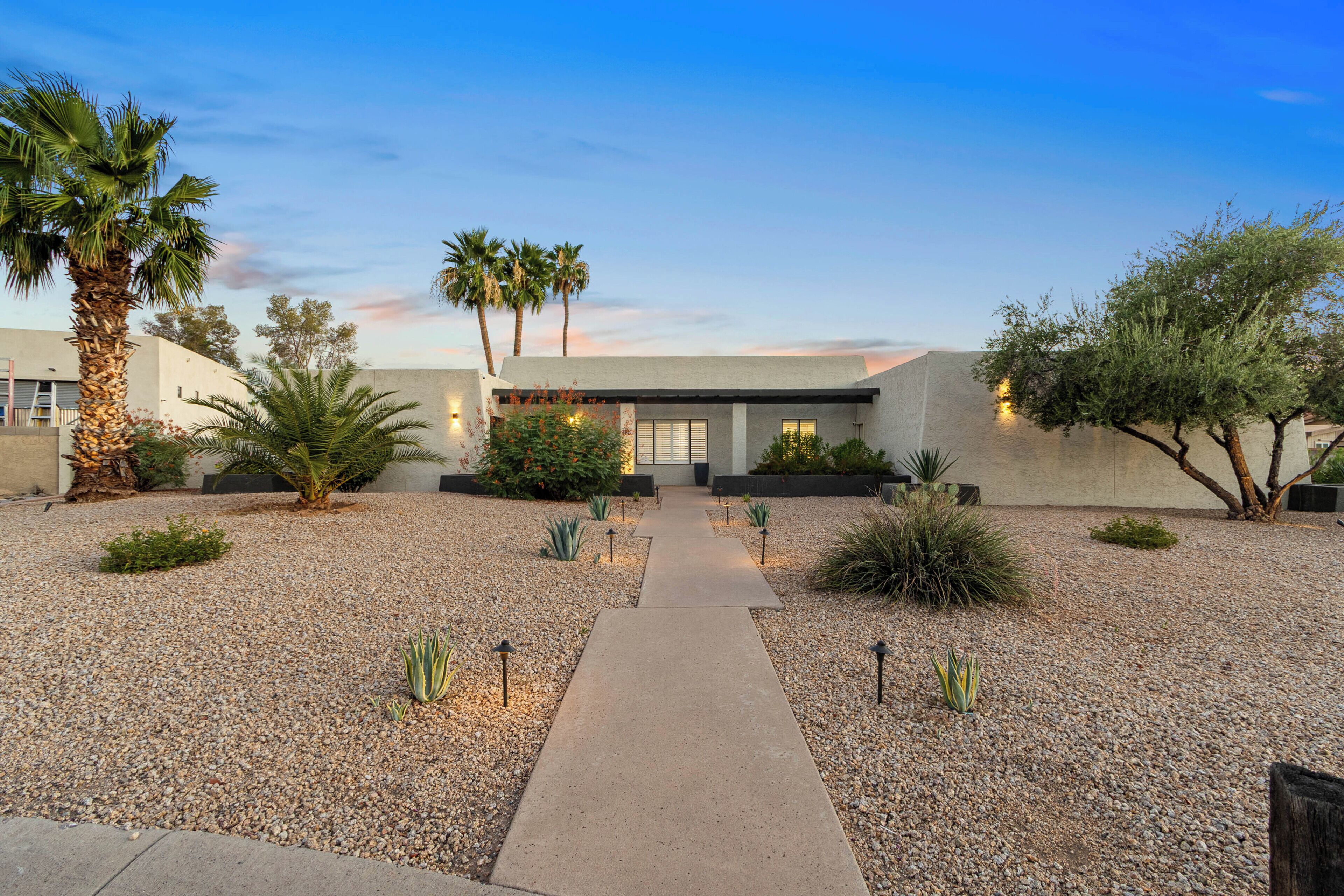 A modern house with a gravel driveway, palm trees, and a pathway leading to the entrance.