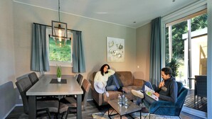 Ein modernes Wohnzimmer mit Esstisch, Sofas und einem großen Fenster mit Vorhängen.