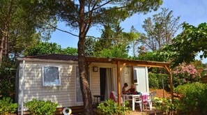 Un piccolo chalet a un piano con veranda, circondato da alberi e arbusti.