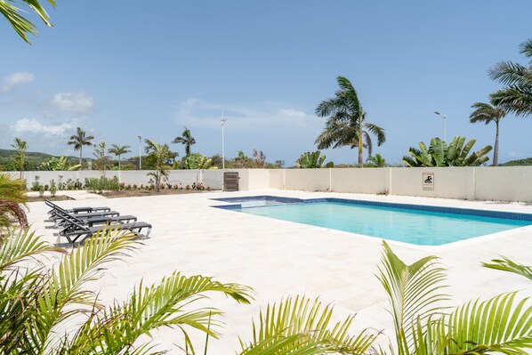 A swimming pool with lounge chairs, surrounded by palm trees and a clear sky.
