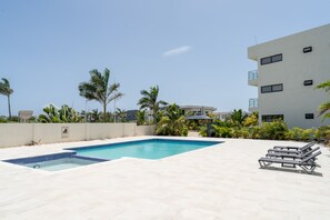 A swimming pool with lounge chairs, surrounded by palm trees and a modern building.