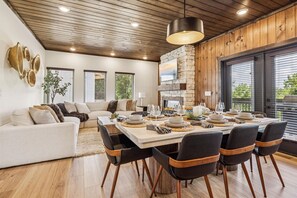A modern dining area with a wooden ceiling, a stone fireplace, and a large window with blinds. - Gorgeous Brand-new Home w Pool Game Room Hot Tub (Pigeon Forge)
