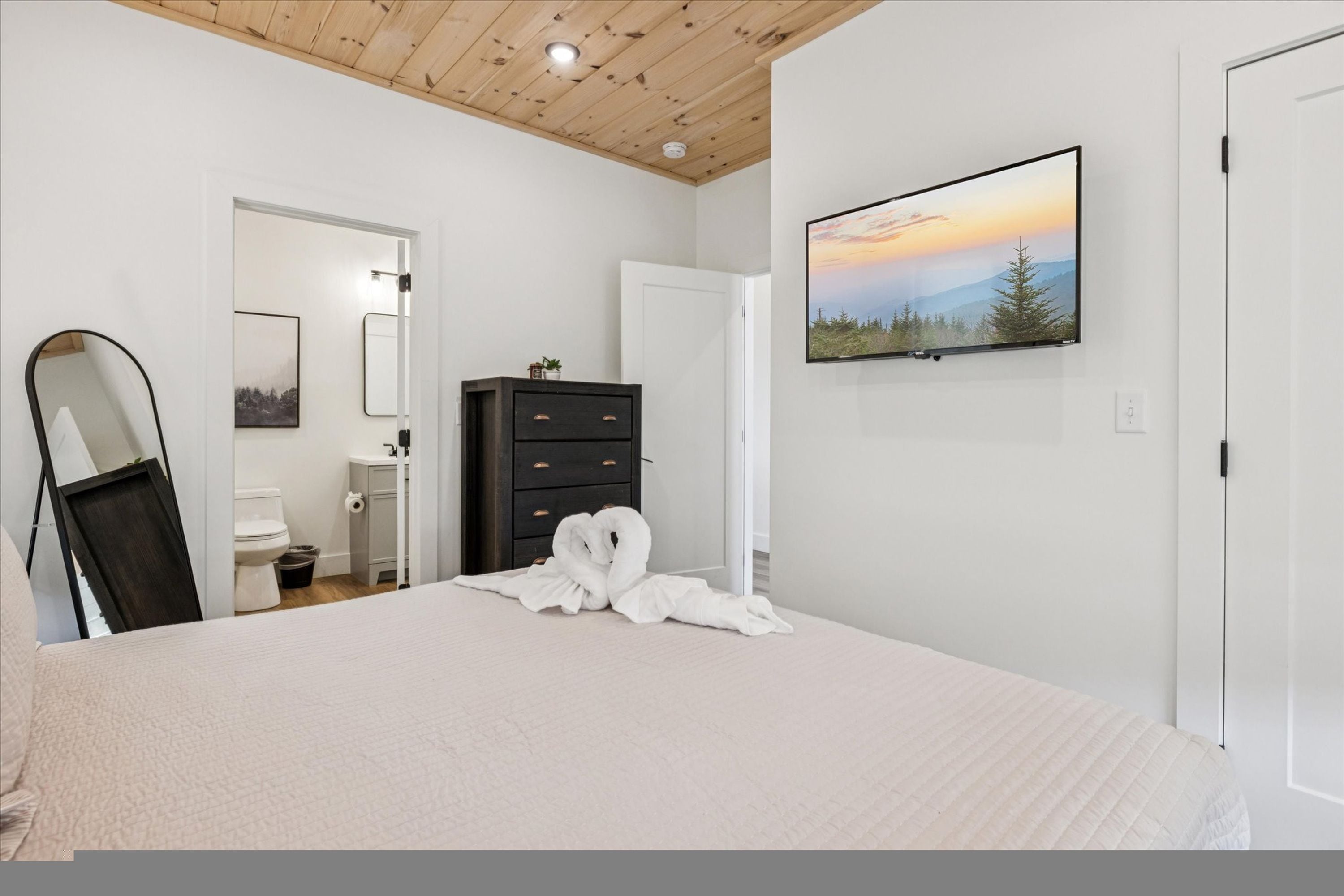 A bedroom with a bed, a dresser, a mirror, and a TV on the wall.