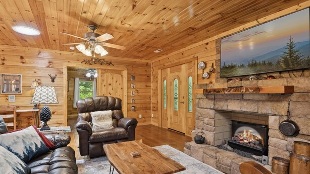 A log cabin interior with a fireplace, leather furniture, and a large TV mounted above it.