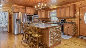 A spacious kitchen with wooden cabinets, a stainless steel refrigerator, a large island with bar stools, and a wooden ceiling.