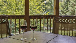 Two wine glasses on a table with a view of trees through a window.