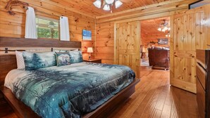 A wooden cabin bedroom with a bed, ceiling fan, and wooden walls.