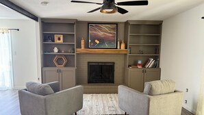 A living room with two armchairs, a fireplace, built-in shelving, and a ceiling fan. - Your Home Away From Home in the Sought Historic Huntridge Hills Neighborhood (Las Vegas)