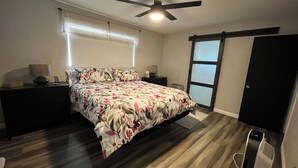 A bedroom with a bed, a nightstand, a desk, a ceiling fan, a window with blinds, and a sliding door. - Your Home Away From Home in the Sought Historic Huntridge Hills Neighborhood (Las Vegas)