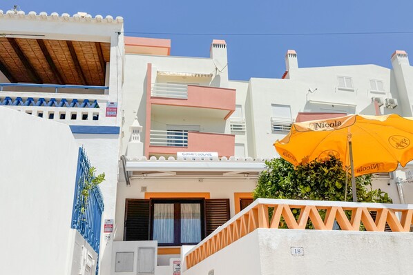 A building with balconies, a sign reading "COSMOS SOLARE," and a yellow umbrella.