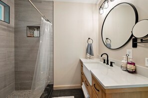 Un baño moderno con ducha, un espejo grande y tocador con artículos de aseo.