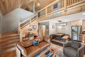 Ein geräumiger Wohnbereich mit einer Holztreppe, einem Ledersofa, einem Esstisch und einer Küche mit modernen Geräten.