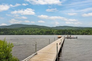 Un muelle de madera que se adentra en un lago tranquilo, con una montaña boscosa al fondo.