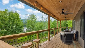Eine Holzterrasse mit Gartenmöbeln, Geländer und Blick auf einen See und Bäume.