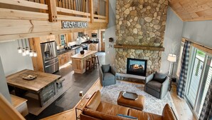 Ein großzügiger, offener Wohnbereich mit Kamin aus Stein, Holzboden und einer Küche mit modernen Geräten.