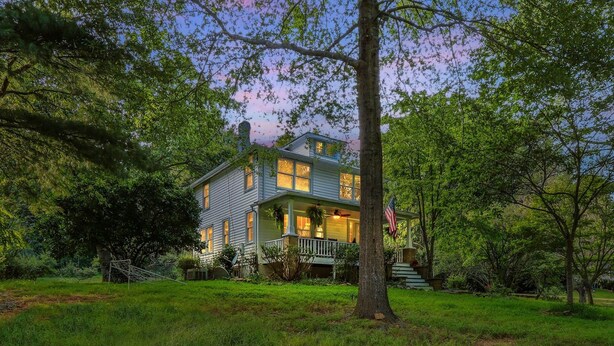A two-story house with a porch, surrounded by trees and grass.